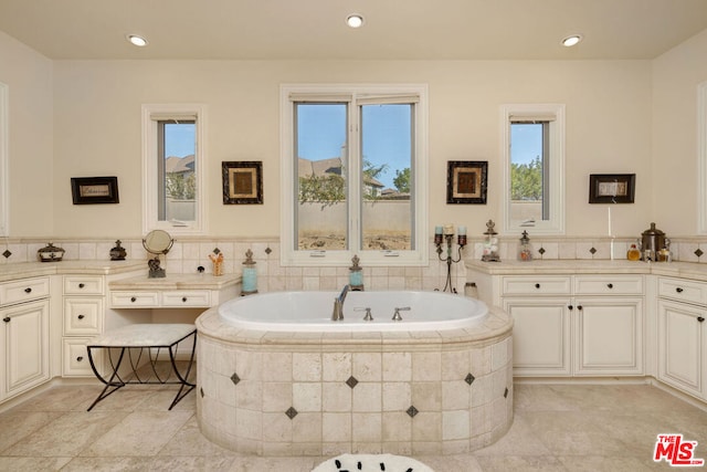 bathroom with tiled tub, vanity, and a healthy amount of sunlight