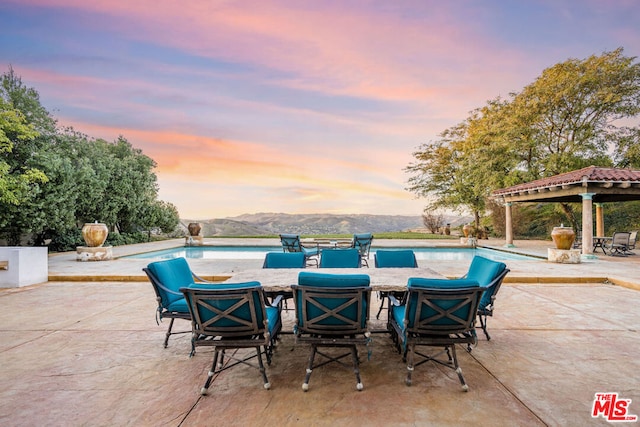 pool at dusk with a mountain view, a gazebo, and a patio