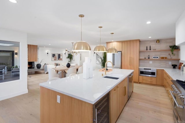 kitchen featuring appliances with stainless steel finishes, sink, beverage cooler, hanging light fixtures, and a kitchen island with sink