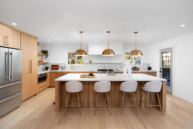 kitchen with appliances with stainless steel finishes, decorative light fixtures, a kitchen island with sink, and a wealth of natural light