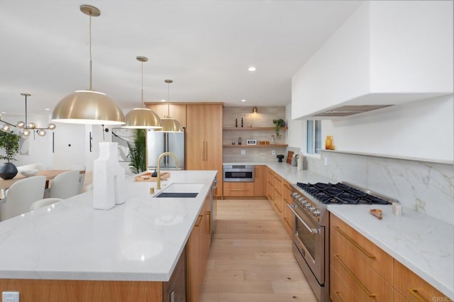 kitchen with sink, a large island, light hardwood / wood-style floors, stainless steel appliances, and light stone countertops