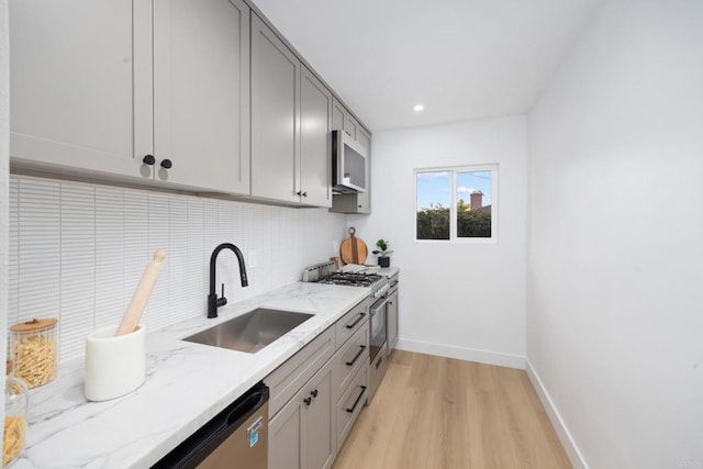 kitchen with sink, backsplash, light stone counters, light hardwood / wood-style floors, and stainless steel appliances