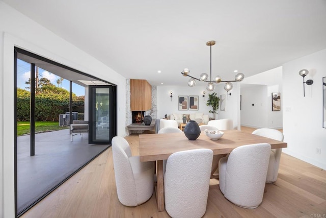 dining space with light hardwood / wood-style flooring, a large fireplace, and a chandelier