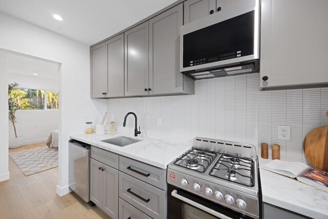 kitchen featuring stainless steel appliances, light stone countertops, sink, and gray cabinetry