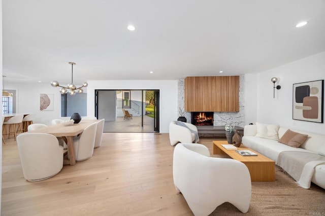 living room featuring an inviting chandelier, a fireplace, and light wood-type flooring