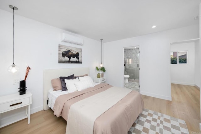 bedroom featuring ensuite bathroom, a wall mounted AC, and light wood-type flooring