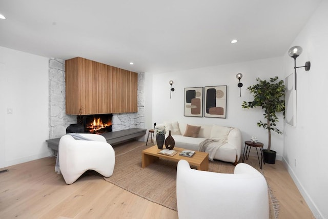 living room with a stone fireplace and light wood-type flooring