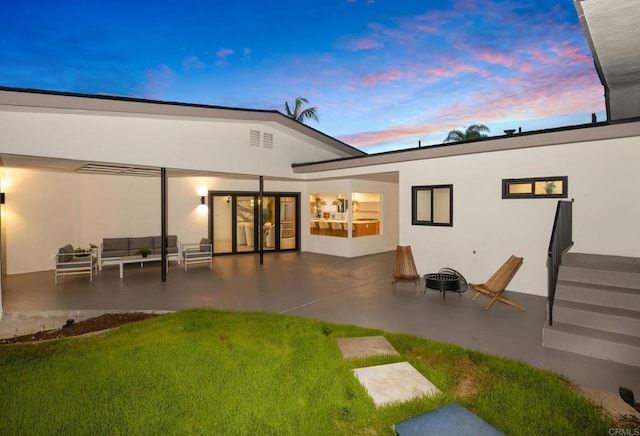 back house at dusk featuring a patio area, a fire pit, and a lawn