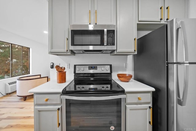 kitchen with light wood-type flooring, appliances with stainless steel finishes, a wall mounted air conditioner, and gray cabinets