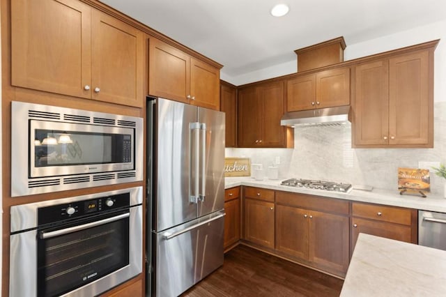 kitchen with dark hardwood / wood-style floors, appliances with stainless steel finishes, tasteful backsplash, and light stone counters