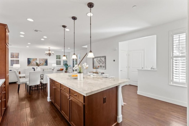 kitchen featuring a center island, light stone countertops, hanging light fixtures, dark wood-type flooring, and a breakfast bar