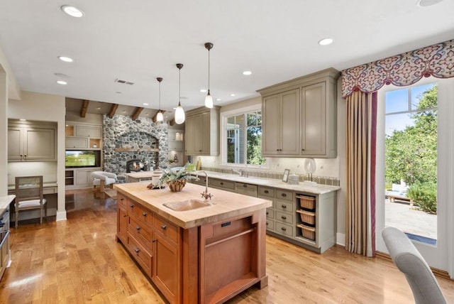 kitchen featuring decorative light fixtures, a center island with sink, butcher block countertops, sink, and a stone fireplace