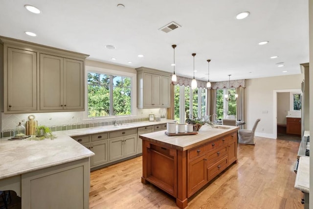 kitchen featuring light hardwood / wood-style floors, backsplash, light stone countertops, a kitchen island, and pendant lighting