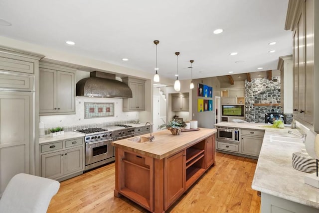 kitchen featuring stainless steel appliances, pendant lighting, backsplash, and wall chimney range hood