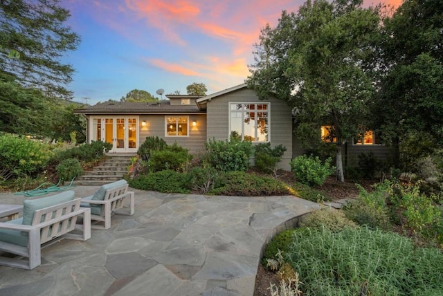 back house at dusk featuring french doors and a patio