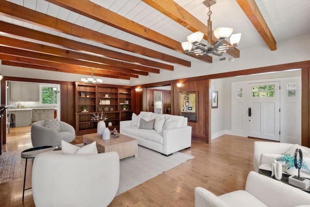 living room featuring beam ceiling, light wood-type flooring, wooden walls, and an inviting chandelier