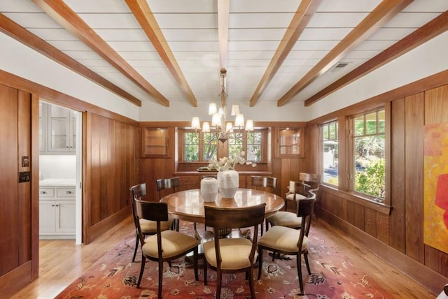 dining area featuring light wood-type flooring, an inviting chandelier, wooden walls, and beamed ceiling