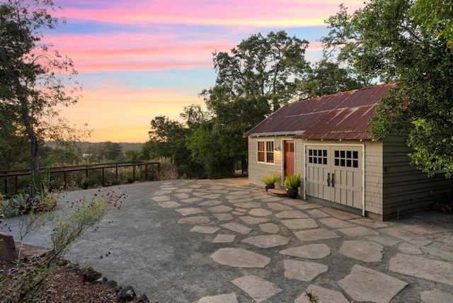 patio terrace at dusk featuring a garage and an outbuilding