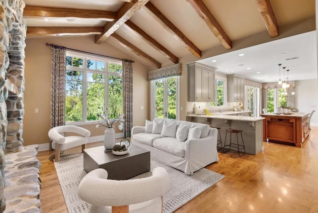 living room featuring plenty of natural light, light hardwood / wood-style flooring, and vaulted ceiling with beams