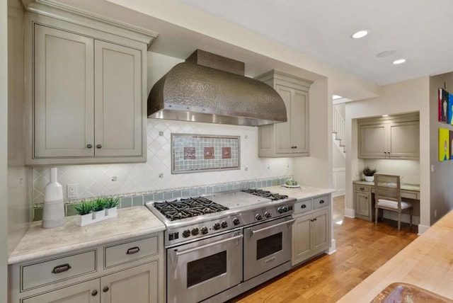 kitchen featuring double oven range, gray cabinetry, decorative backsplash, light wood-type flooring, and custom range hood