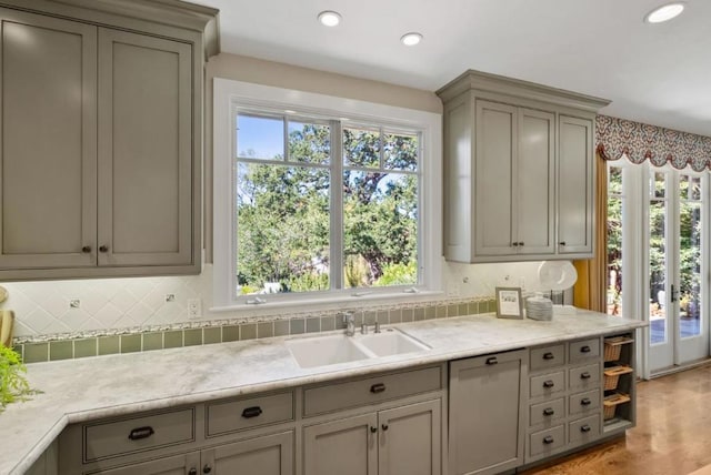 kitchen with gray cabinetry, french doors, tasteful backsplash, sink, and light hardwood / wood-style flooring