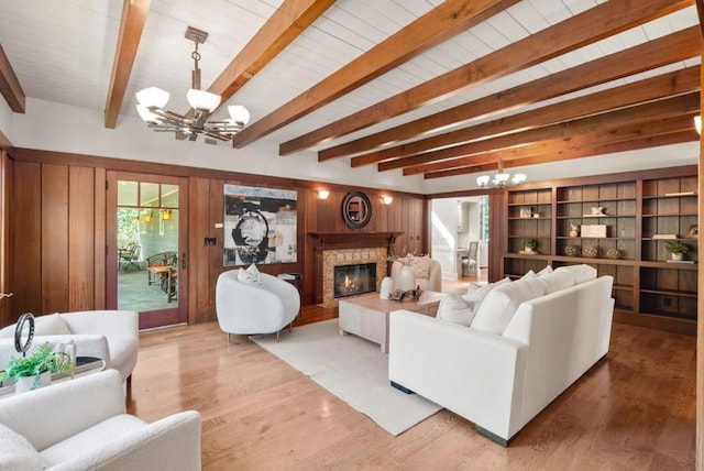 living room with a notable chandelier, a fireplace, wood walls, beam ceiling, and light hardwood / wood-style flooring