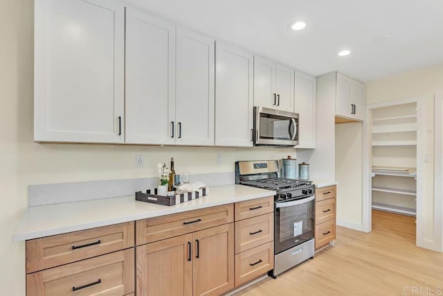 kitchen featuring appliances with stainless steel finishes, light brown cabinetry, light hardwood / wood-style floors, and white cabinets