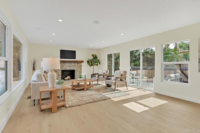 living room with a stone fireplace, a healthy amount of sunlight, and light wood-type flooring