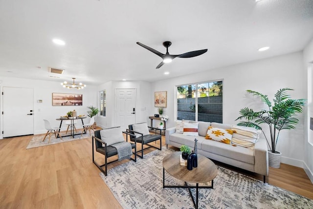 living room featuring ceiling fan with notable chandelier and light hardwood / wood-style flooring