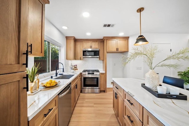 kitchen with stainless steel appliances, decorative light fixtures, light wood-type flooring, light stone counters, and sink