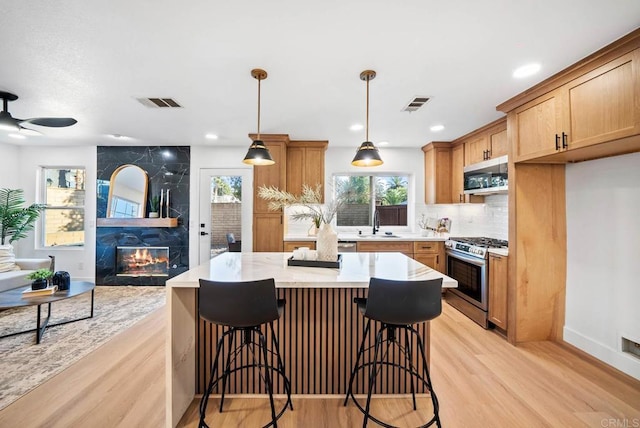 kitchen with a center island, pendant lighting, sink, light hardwood / wood-style flooring, and stainless steel appliances