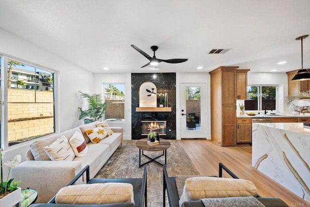 living room with light hardwood / wood-style floors, sink, a premium fireplace, and a healthy amount of sunlight