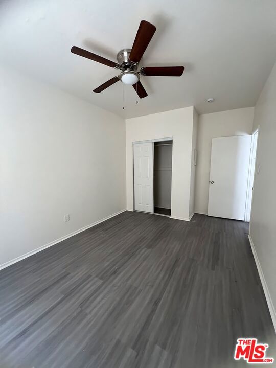 unfurnished bedroom with ceiling fan, a closet, and dark wood-type flooring