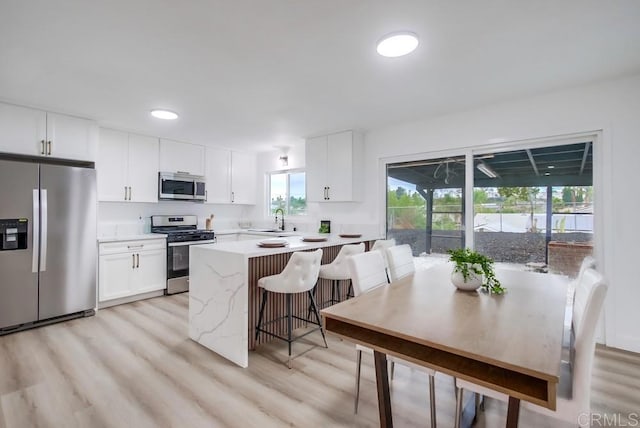 kitchen featuring a breakfast bar, sink, light wood-type flooring, appliances with stainless steel finishes, and white cabinets