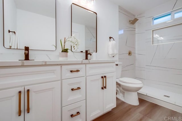 bathroom with toilet, a tile shower, hardwood / wood-style floors, and vanity