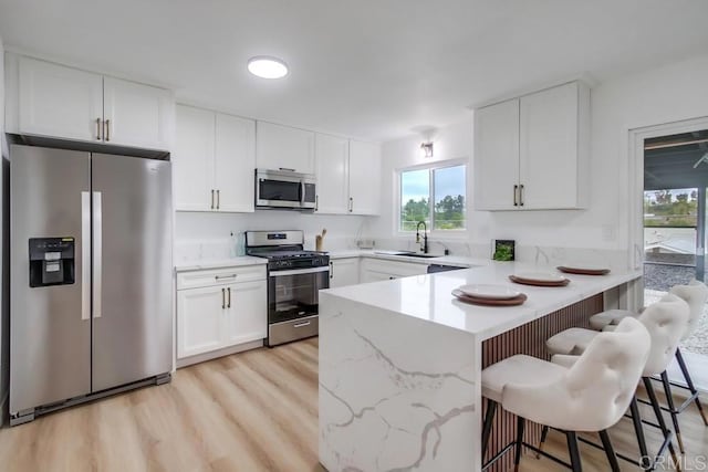 kitchen with kitchen peninsula, stainless steel appliances, white cabinets, a breakfast bar, and sink