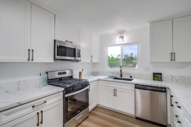 kitchen with white cabinetry, appliances with stainless steel finishes, light stone countertops, light hardwood / wood-style flooring, and sink