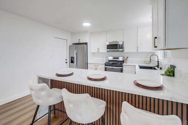 kitchen with white cabinetry, stainless steel appliances, sink, kitchen peninsula, and a breakfast bar