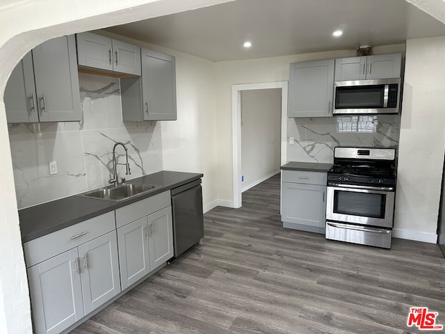 kitchen featuring stainless steel appliances, gray cabinetry, backsplash, dark wood-type flooring, and sink