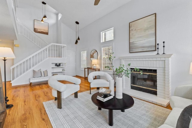 living room featuring hardwood / wood-style flooring, ceiling fan, a fireplace, and a high ceiling