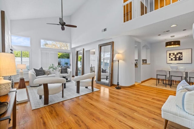 living room with a towering ceiling, light hardwood / wood-style flooring, and ceiling fan