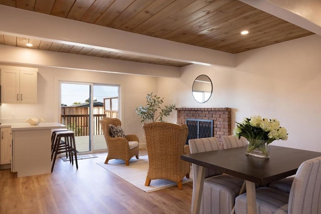 dining area featuring beamed ceiling, wood ceiling, a fireplace, and light hardwood / wood-style floors