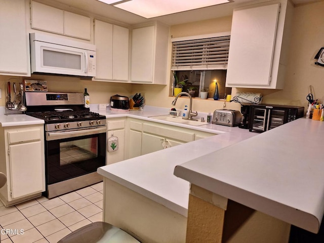 695 County Square Dr Unit 13, Ventura, CA 93003 - kitchen featuring white cabinets, sink, kitchen peninsula, light tile patterned floors, and stainless steel range with gas stovetop