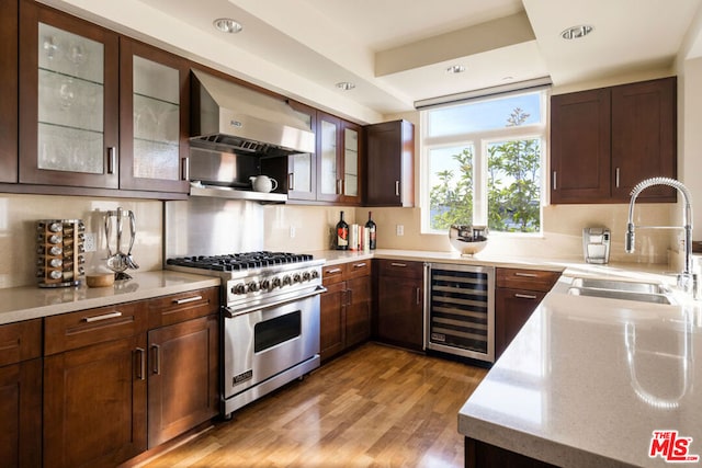 kitchen with beverage cooler, wall chimney exhaust hood, wood-type flooring, sink, and luxury range