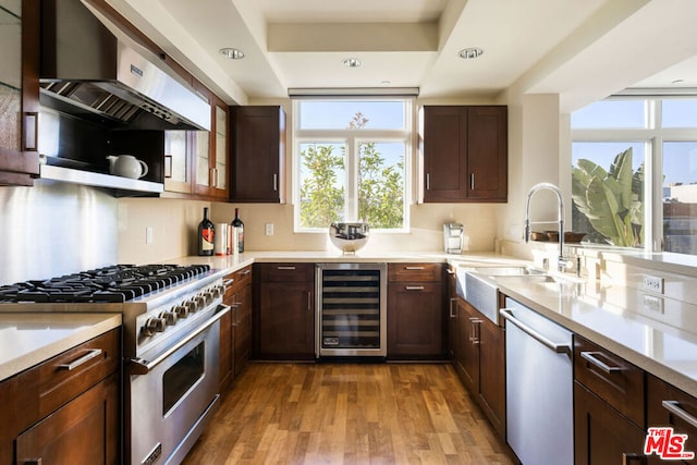 kitchen with beverage cooler, appliances with stainless steel finishes, sink, light hardwood / wood-style flooring, and range hood