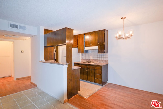 kitchen featuring white fridge, backsplash, a notable chandelier, stainless steel gas cooktop, and hanging light fixtures