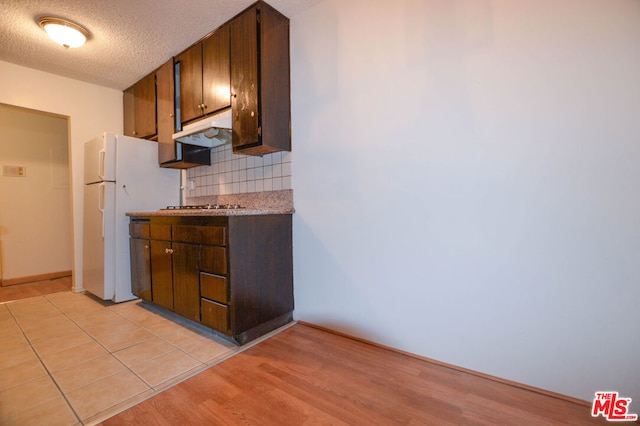 kitchen with backsplash, white fridge, a textured ceiling, and dark brown cabinetry