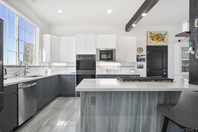 kitchen with tasteful backsplash, beamed ceiling, gray cabinetry, stainless steel appliances, and white cabinets