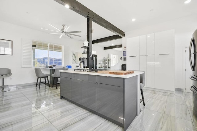 kitchen with gray cabinets, a center island, beam ceiling, white cabinetry, and a breakfast bar area