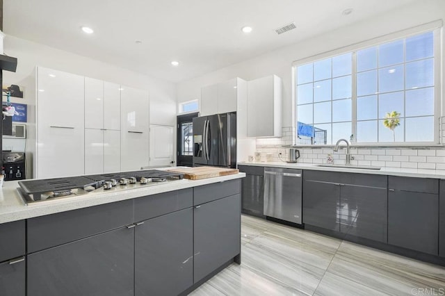 kitchen with white cabinets, appliances with stainless steel finishes, decorative backsplash, sink, and light tile patterned floors